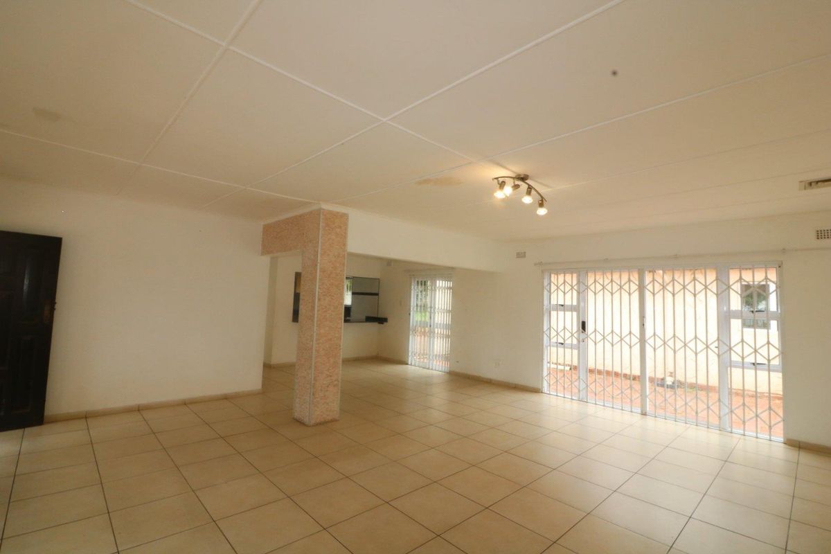 Spacious open-plan living area featuring tiled flooring, a structural pillar, and sliding doors with security gates leading to the exterior.