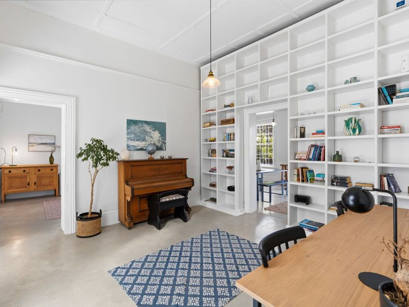 A bright living area featuring extensive built-in floor-to-ceiling shelving, polished concrete floors, and a classic coffered ceiling, offering a versatile and well-maintained space.