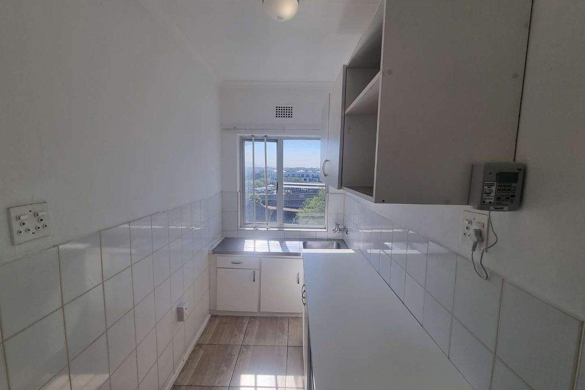 A compact, functional kitchen featuring built-in cabinetry, a stainless steel sink, tiled splashbacks, and tiled flooring, offering a clean and practical workspace.