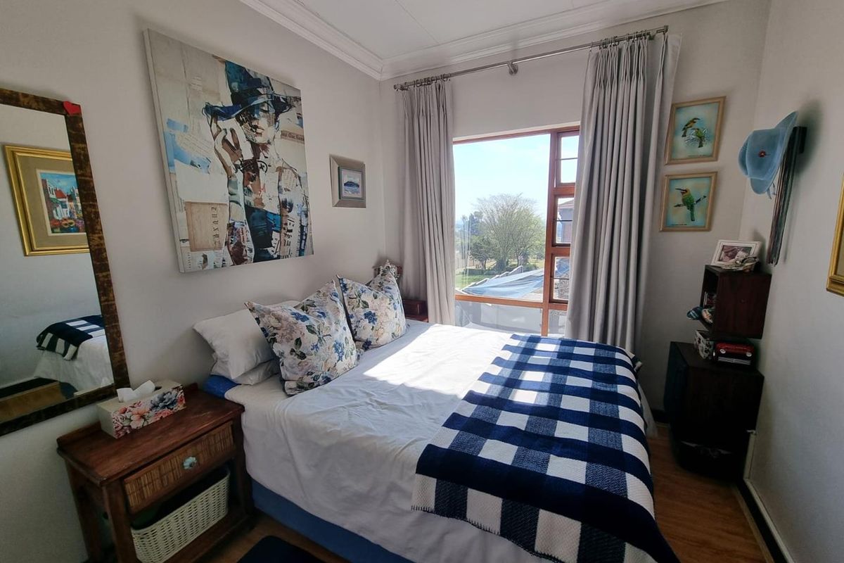 A cozy bedroom featuring laminate flooring, decorative cornice detailing, and a window providing natural light and exterior views.