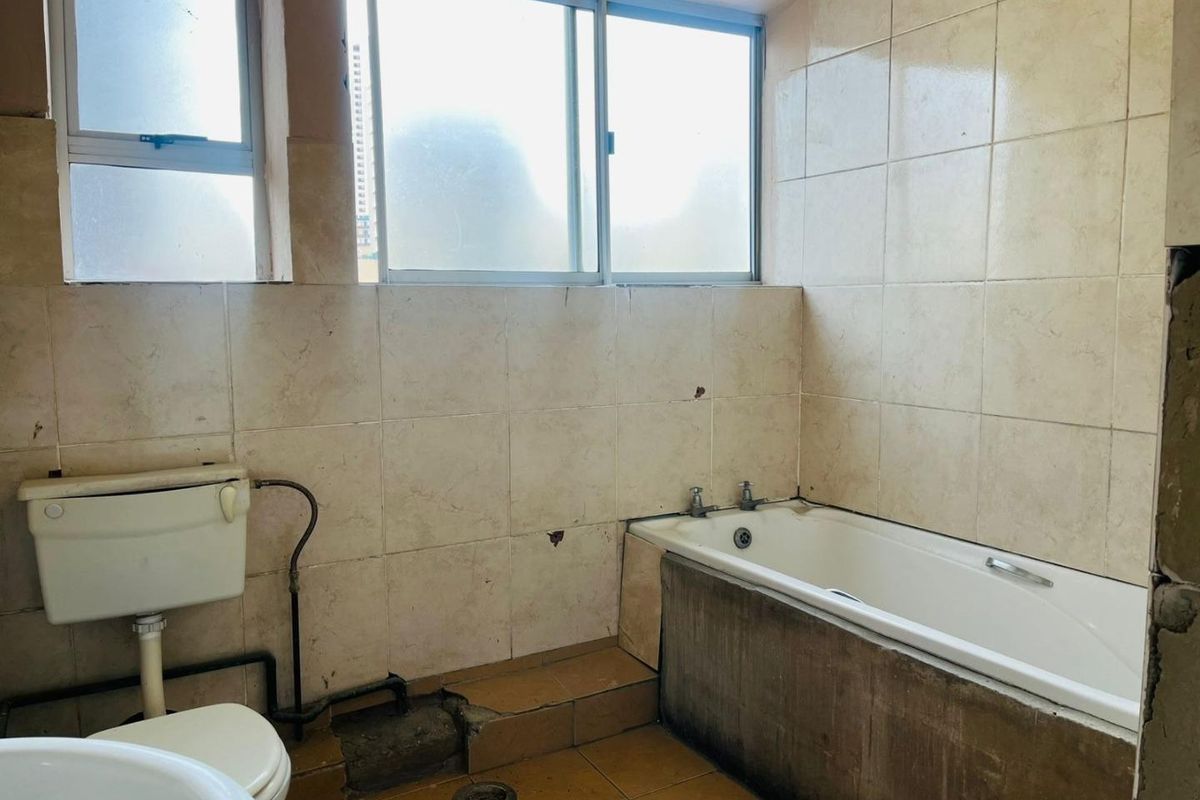 A dated bathroom featuring a bathtub, toilet, and tiled finishes, currently requiring significant renovation and repair to the flooring and wall surfaces.