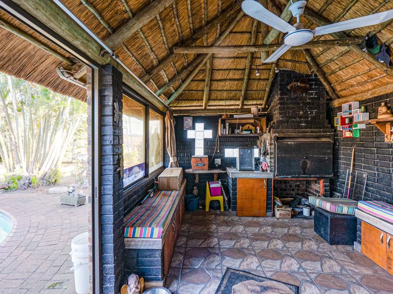 Covered outdoor patio area featuring a thatched roof, built-in braai, and direct access to the pool area.