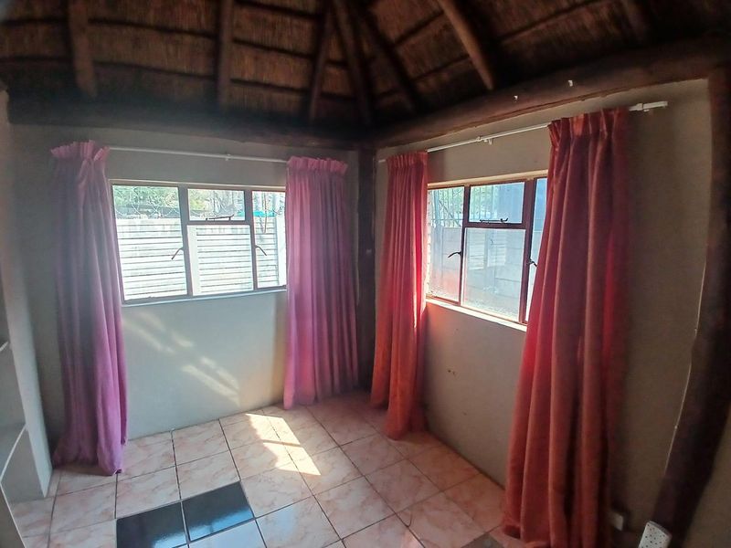 A vacant bedroom featuring a traditional thatched roof with exposed timber beams and tiled flooring, offering a rustic cottage aesthetic.
