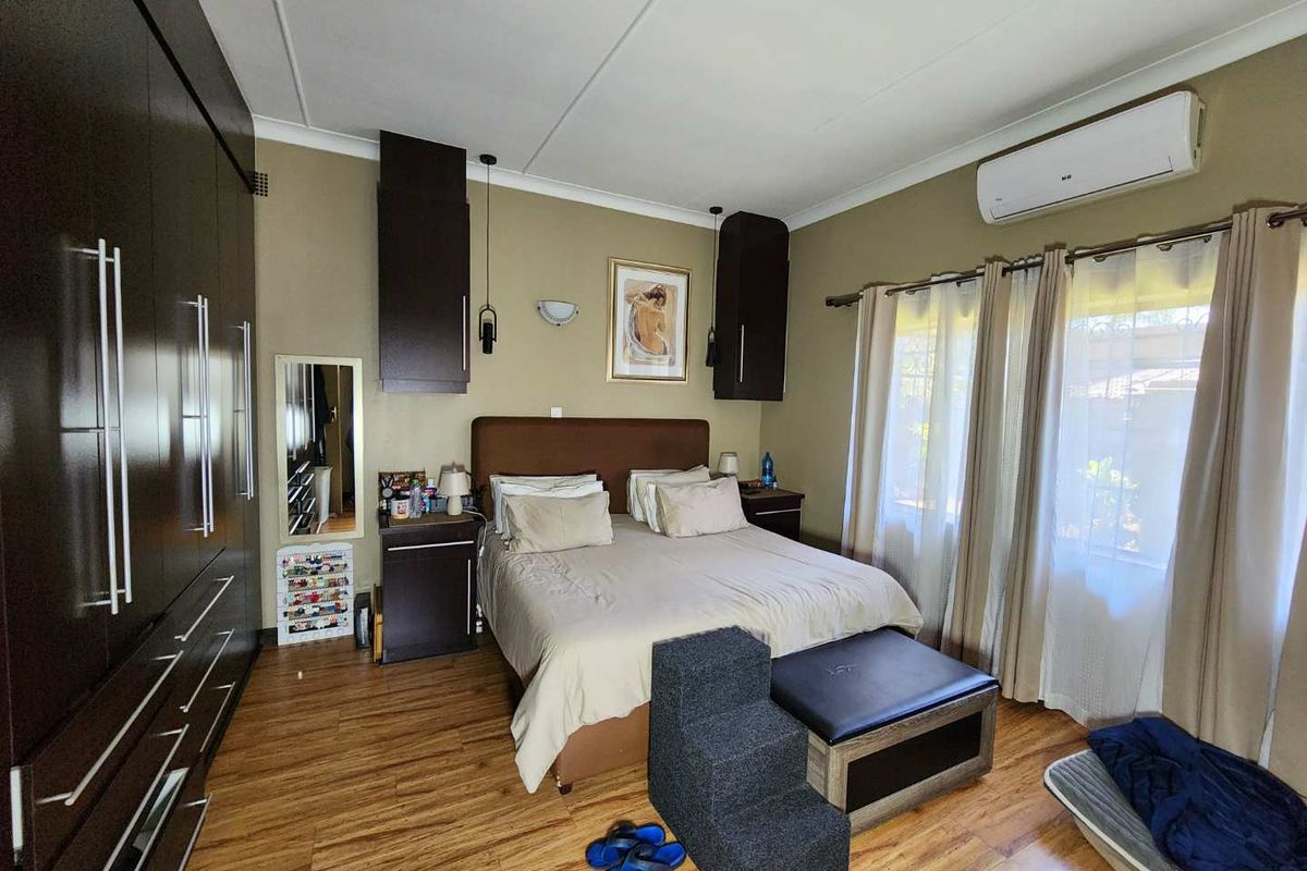 A well-maintained bedroom featuring laminate flooring, extensive built-in cabinetry, and a wall-mounted air conditioning unit.
