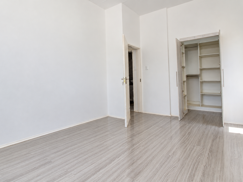 A bright, empty bedroom featuring light-toned laminate flooring and a built-in wardrobe with shelving.