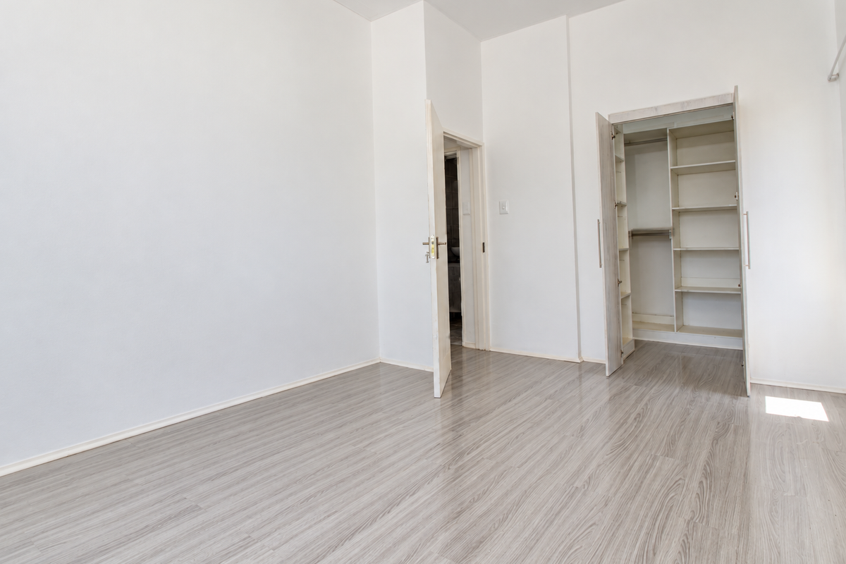 A bright, empty bedroom featuring light-toned laminate flooring and a built-in wardrobe with shelving.