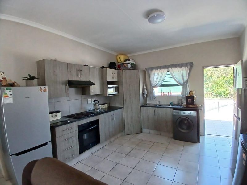 A functional kitchen featuring wood-look cabinetry, dark countertops, built-in appliances, and tiled flooring with direct access to an outdoor area.