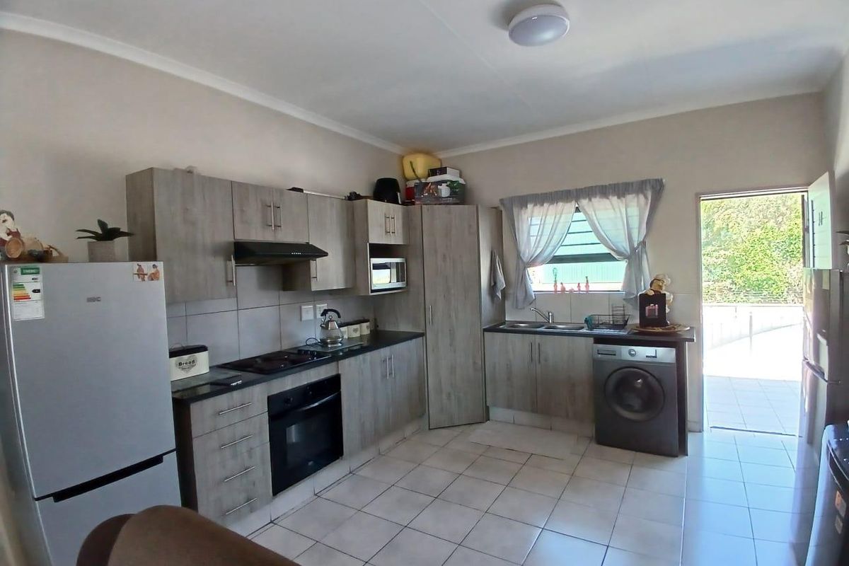 A functional kitchen featuring wood-look cabinetry, dark countertops, built-in appliances, and tiled flooring with direct access to an outdoor area.