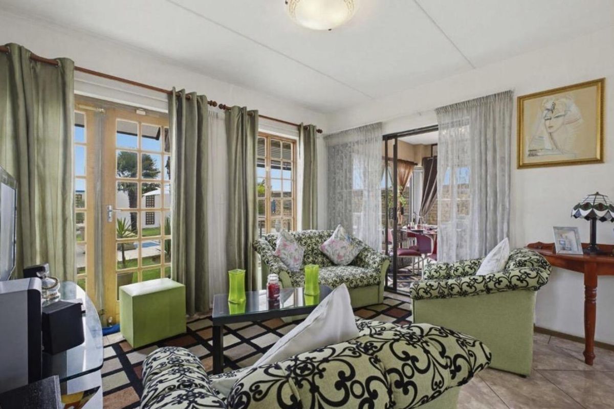 A bright living room featuring tiled flooring, large french doors, and a sliding glass door providing access to the outdoor patio area.