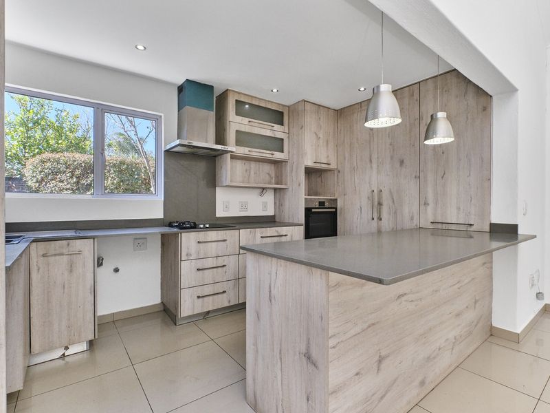 Modern kitchen featuring light wood-grain cabinetry, stone countertops, a central island, and integrated appliances, finished with neutral floor tiles and recessed lighting.