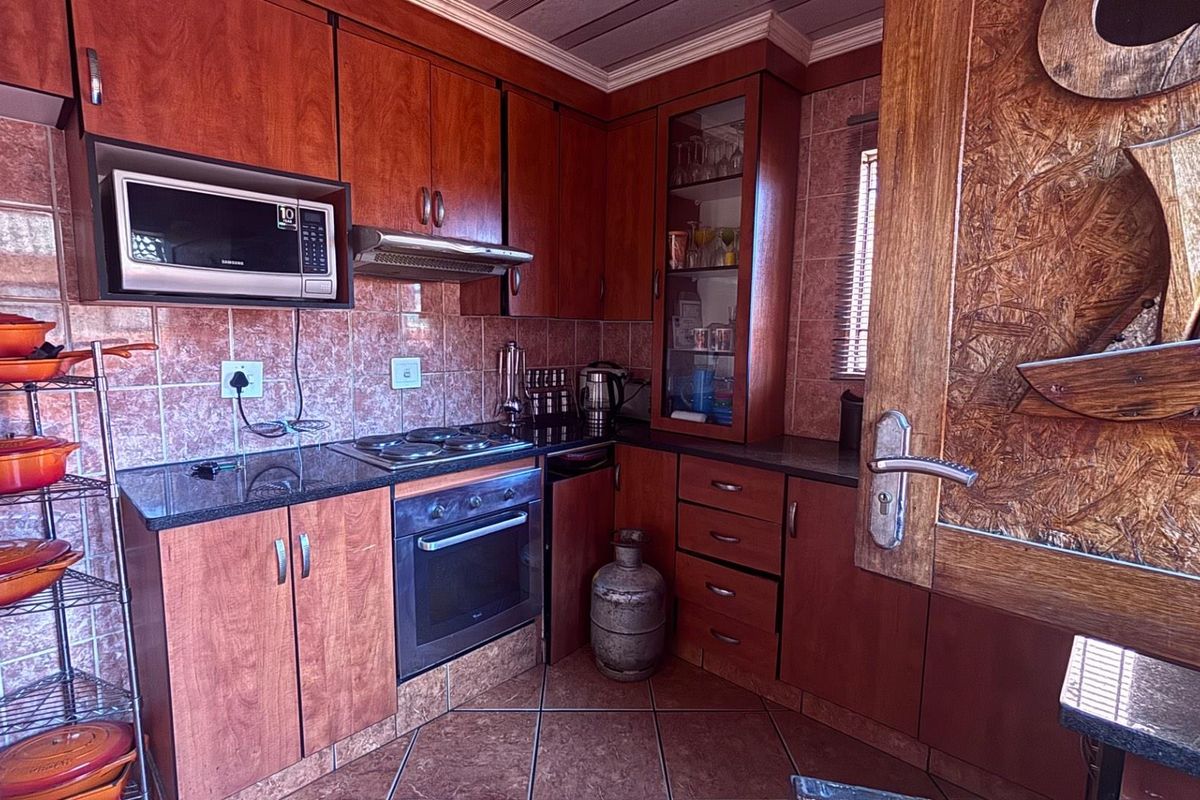 A compact kitchen featuring wood-veneer cabinetry, granite countertops, a built-in oven, electric hob, and an integrated extractor fan.
