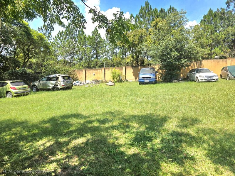 A large, open garden area featuring a perimeter wall with electric fencing, currently used for vehicle storage with some debris present.