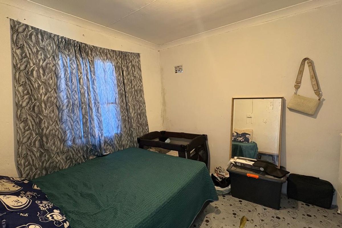 A bedroom featuring a window with curtains and standard wall finishes, requiring cosmetic updates to improve the overall condition.