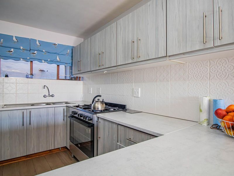 A functional kitchen featuring light wood-grain cabinetry, stone-look countertops, a gas hob, and a tiled backsplash.