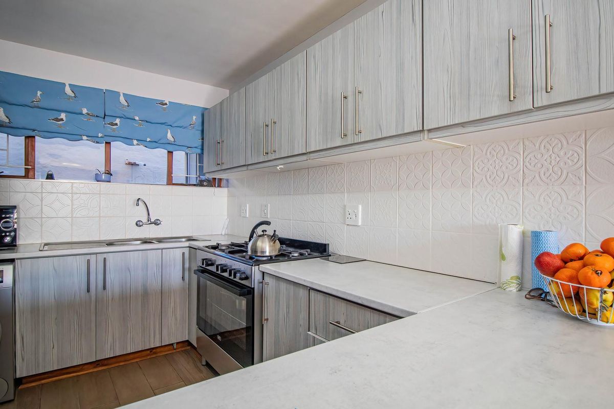 A functional kitchen featuring light wood-grain cabinetry, stone-look countertops, a gas hob, and a tiled backsplash.