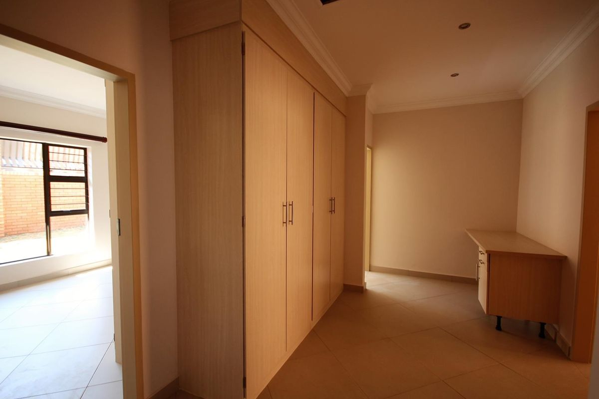A spacious bedroom featuring light wood-finish built-in cupboards, a matching built-in desk, tiled flooring, and recessed ceiling lighting.