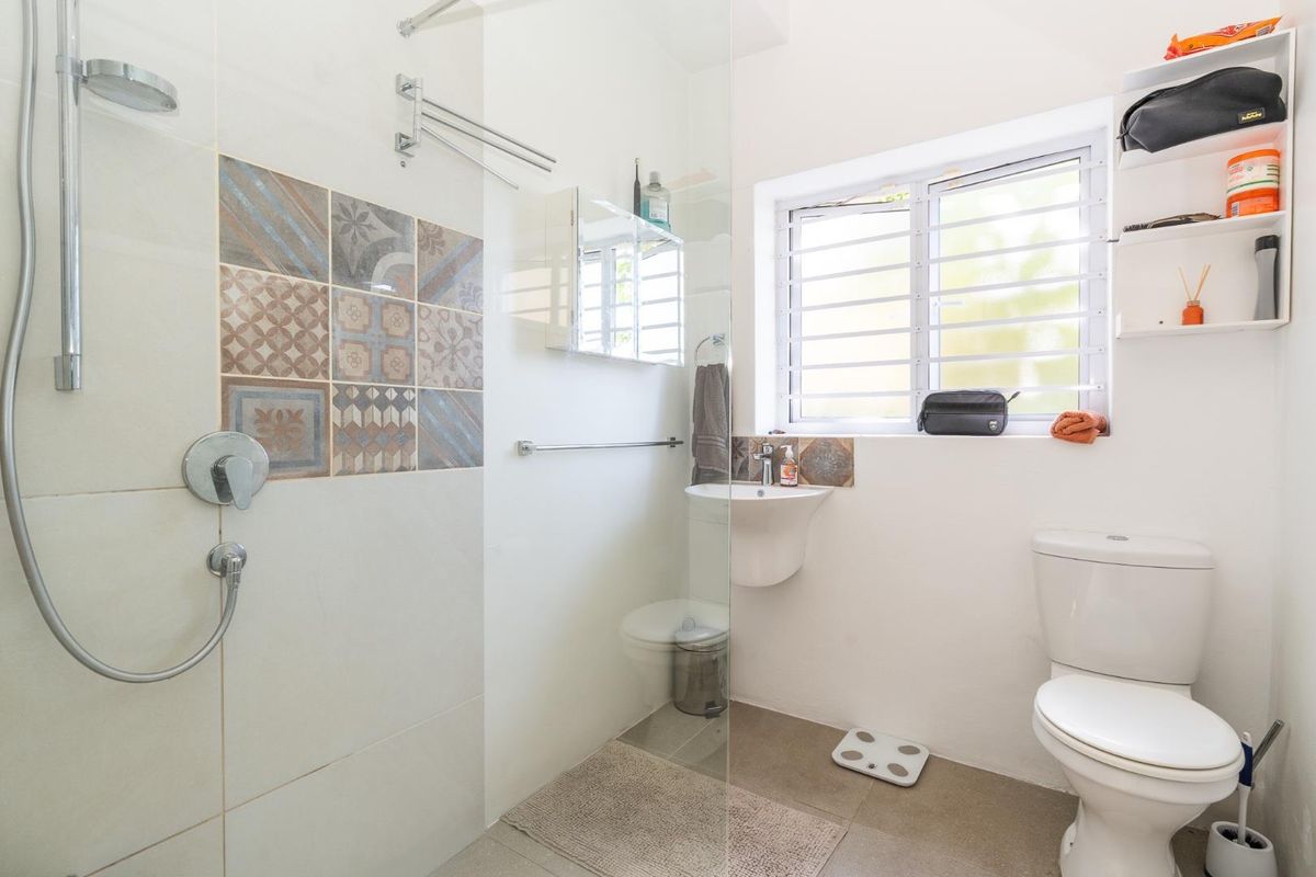 A compact, modern bathroom featuring a glass-enclosed walk-in shower, wall-mounted basin, and toilet, accented with decorative patterned wall tiles.