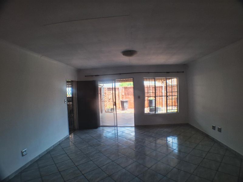 An empty living room featuring tiled flooring, a sliding glass door leading to the patio, and security bars on the windows.