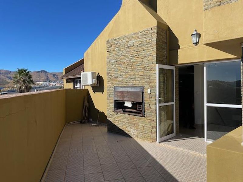 Spacious outdoor patio featuring a built-in stone-clad braai, tiled flooring, and direct access to the interior living area.