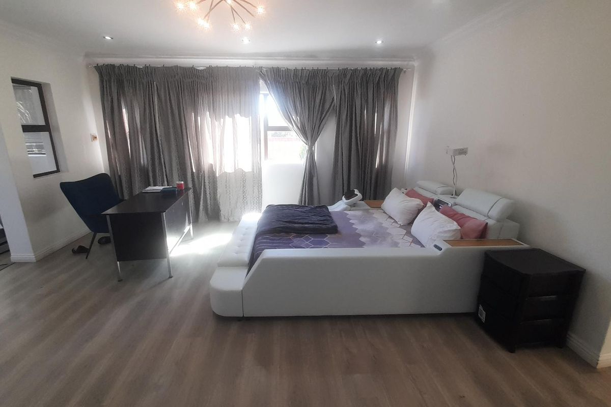 Spacious bedroom featuring light wood-look flooring, recessed ceiling lighting, and large windows with floor-to-ceiling curtains.