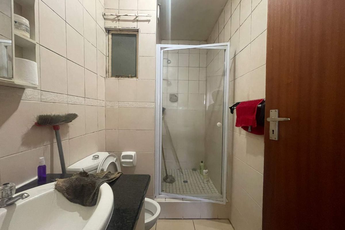 A compact bathroom featuring a shower enclosure, vanity with basin, and toilet, finished with neutral wall tiles and tiled flooring.