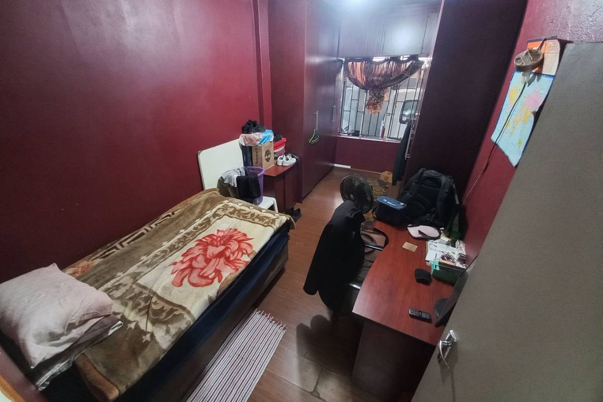 A compact bedroom featuring built-in cupboards, dark red wall paint, and laminate flooring, offering a functional space for a single occupant.
