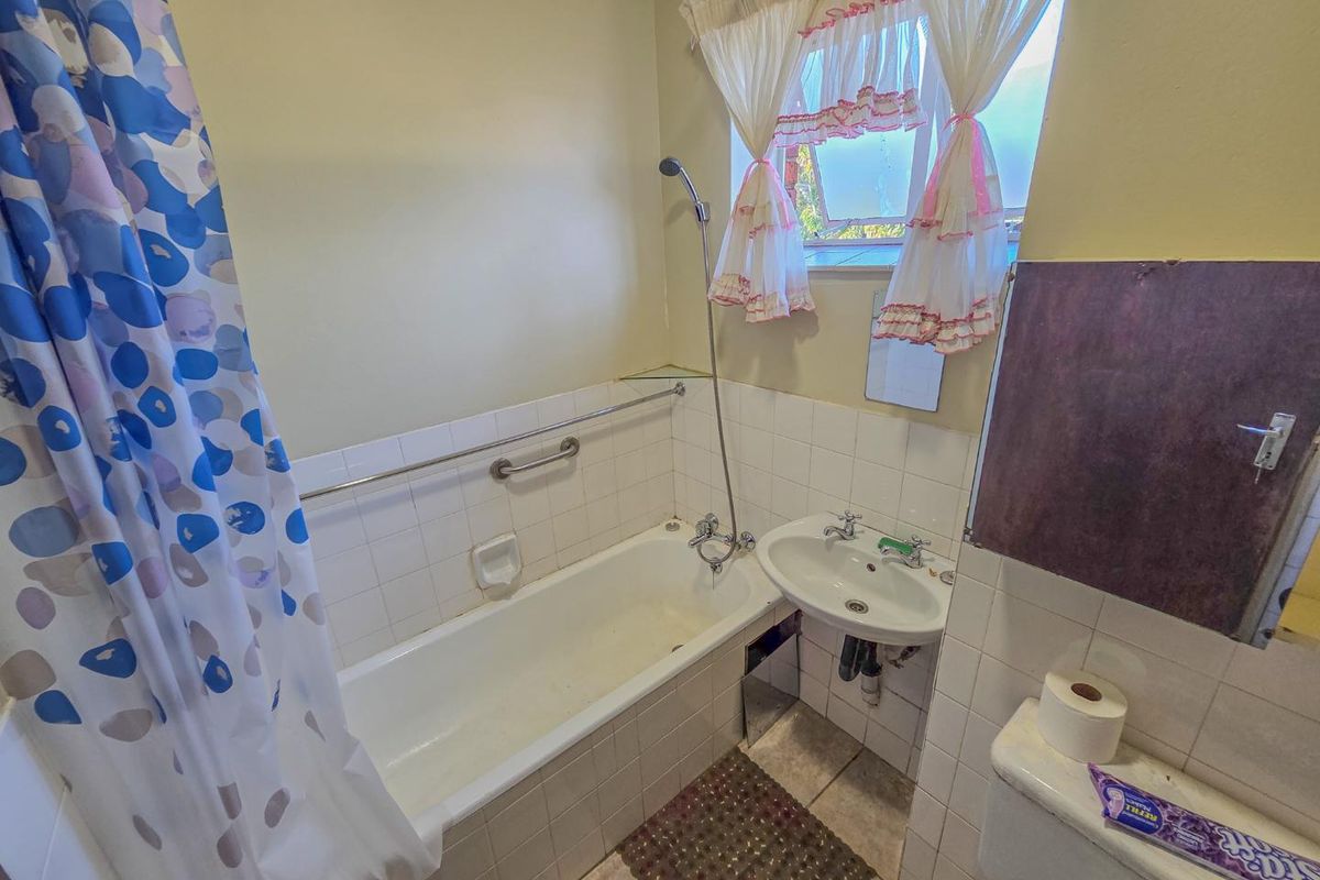 A functional bathroom featuring a bathtub with shower attachment, pedestal basin, and toilet, requiring cosmetic updates to modernize the space.
