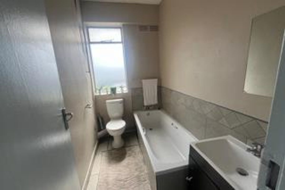 A functional bathroom featuring a standard bathtub, toilet, and vanity basin with neutral wall finishes and natural light from a window.