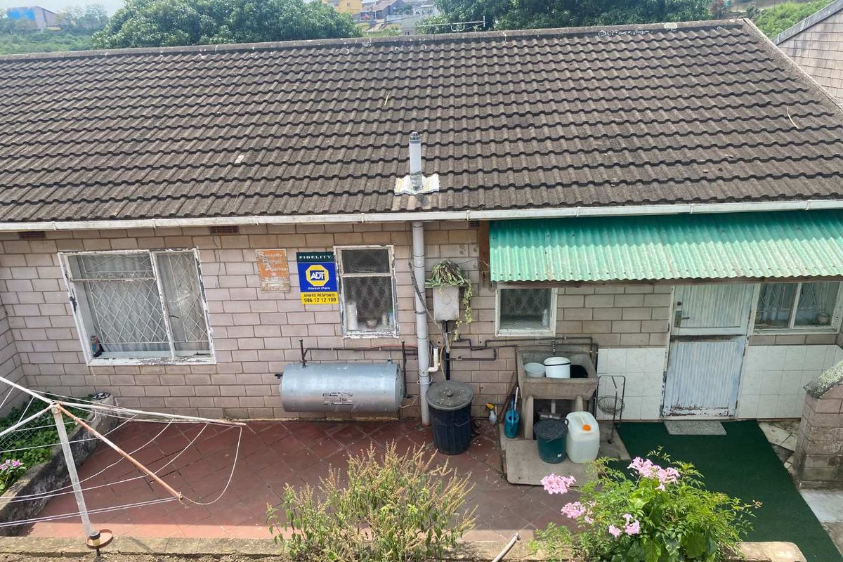 Rear exterior view of the property featuring brick masonry walls, a concrete tile roof, security bars, and an external utility sink area.