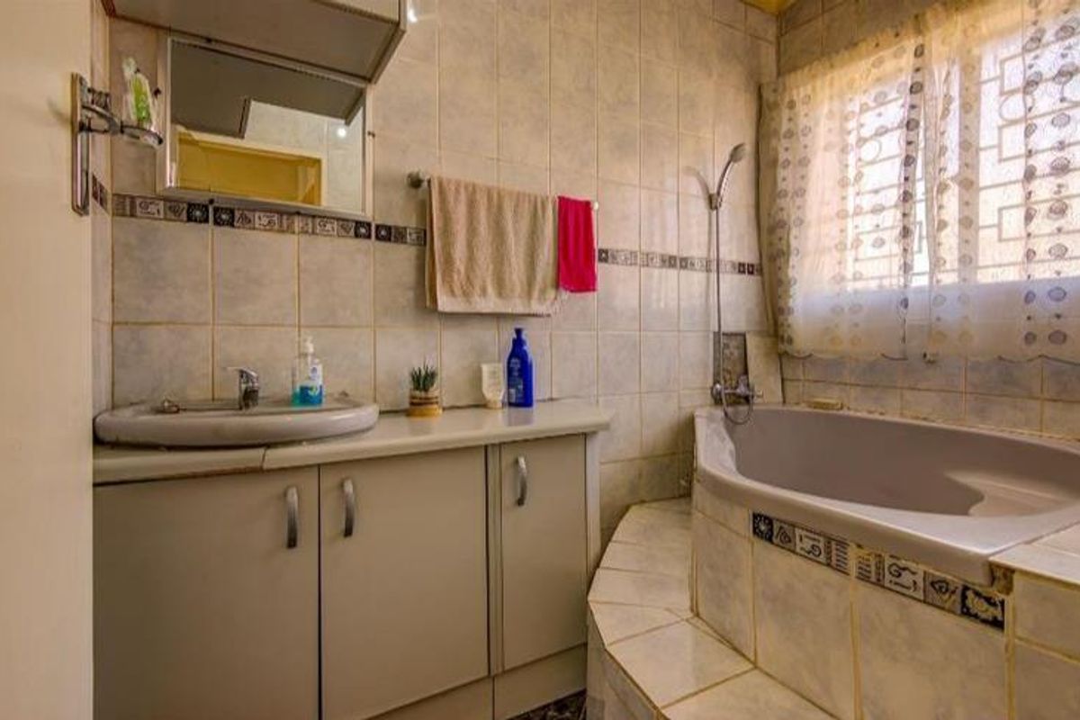 A dated bathroom featuring a built-in bathtub, vanity cabinet with basin, and tiled finishes throughout, offering potential for a modern renovation.