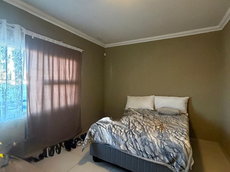 A functional bedroom featuring neutral wall tones, tiled flooring, and a simple ceiling light fixture, offering a clean and straightforward living space.