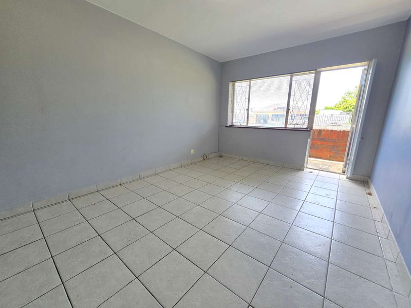 An empty living room featuring tiled flooring and direct access to an outdoor balcony area through a security door.