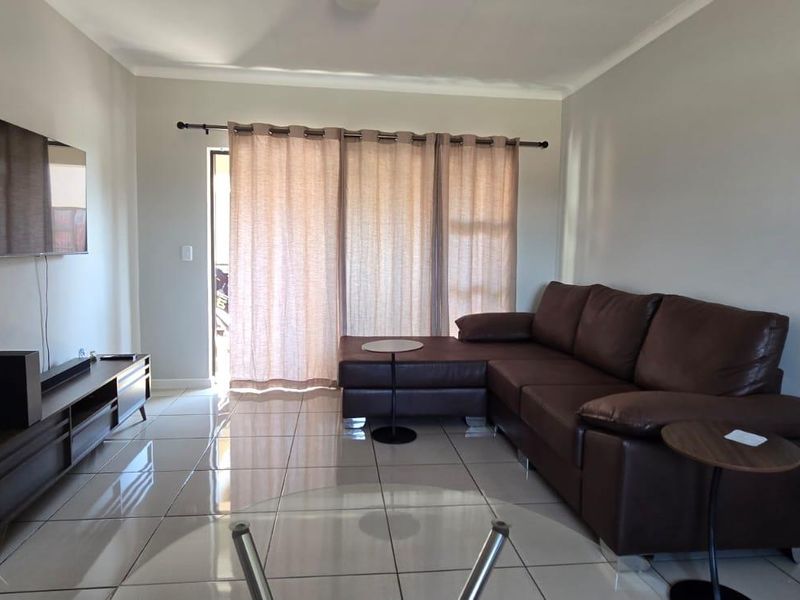 A well-maintained living room featuring neutral tiled flooring and a sliding glass door that provides access to the outdoor area.