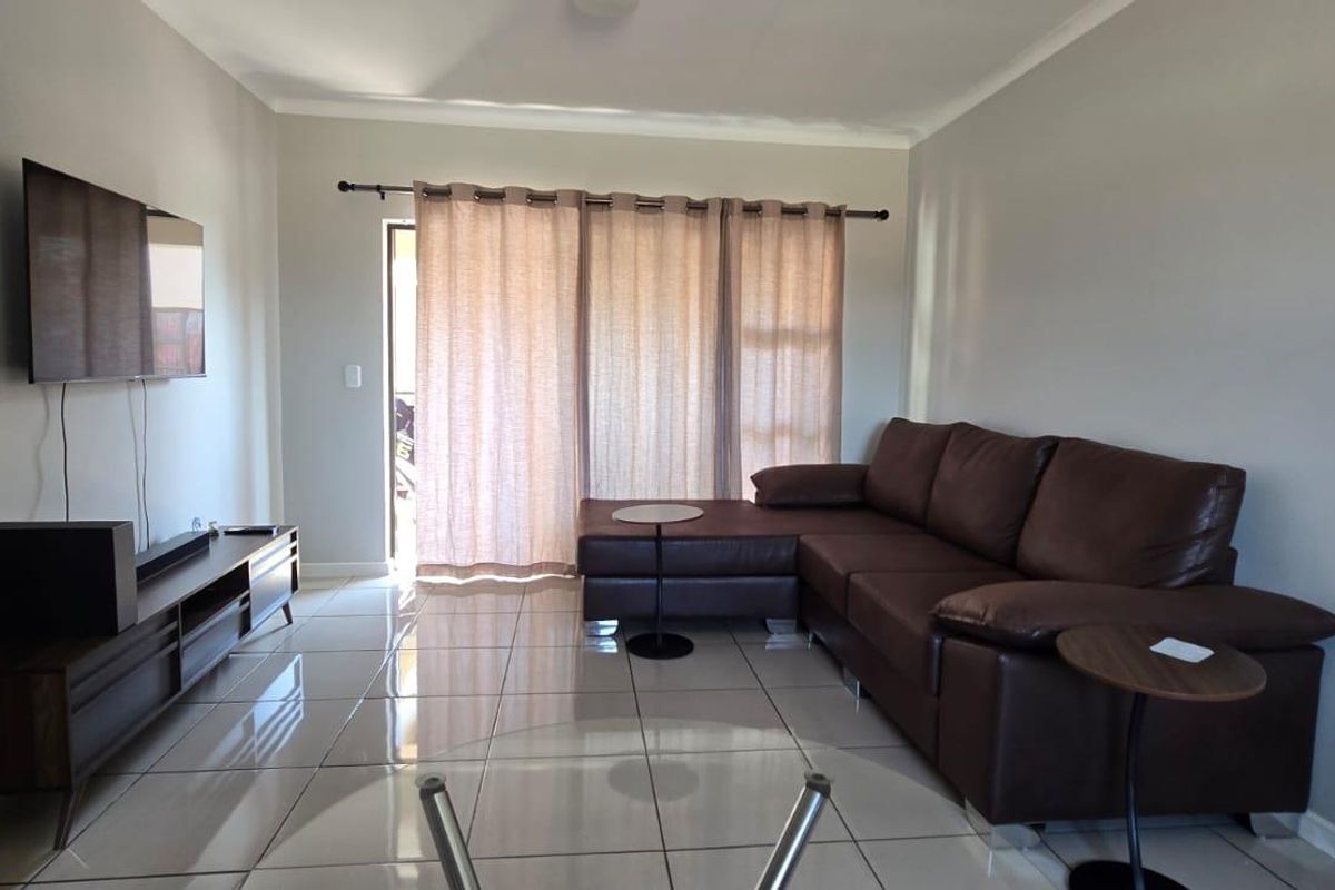 A well-maintained living room featuring neutral tiled flooring and a sliding glass door that provides access to the outdoor area.