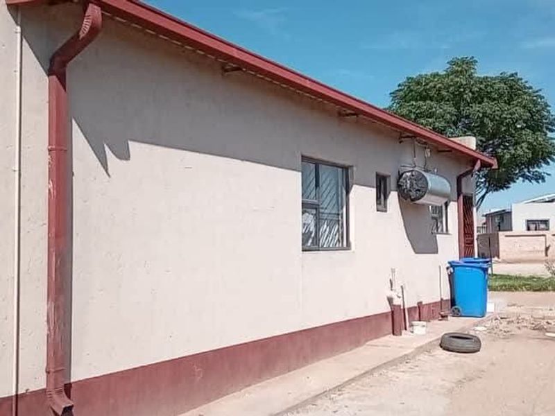 Rear exterior view of the property showing the building facade, guttering, window security bars, and an external electric geyser.
