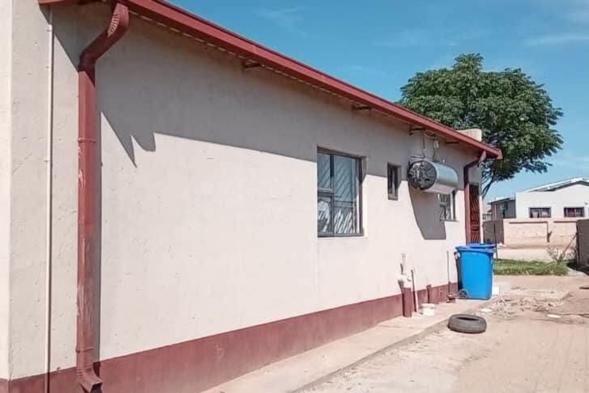 Rear exterior view of the property showing the building facade, guttering, window security bars, and an external electric geyser.