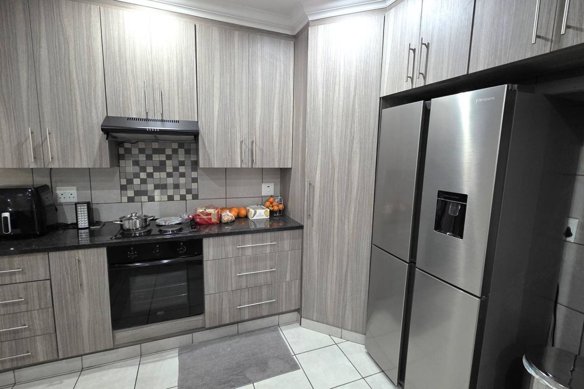 Modern kitchen featuring light wood-grain cabinetry, dark granite countertops, a built-in oven, extractor fan, and tiled flooring.