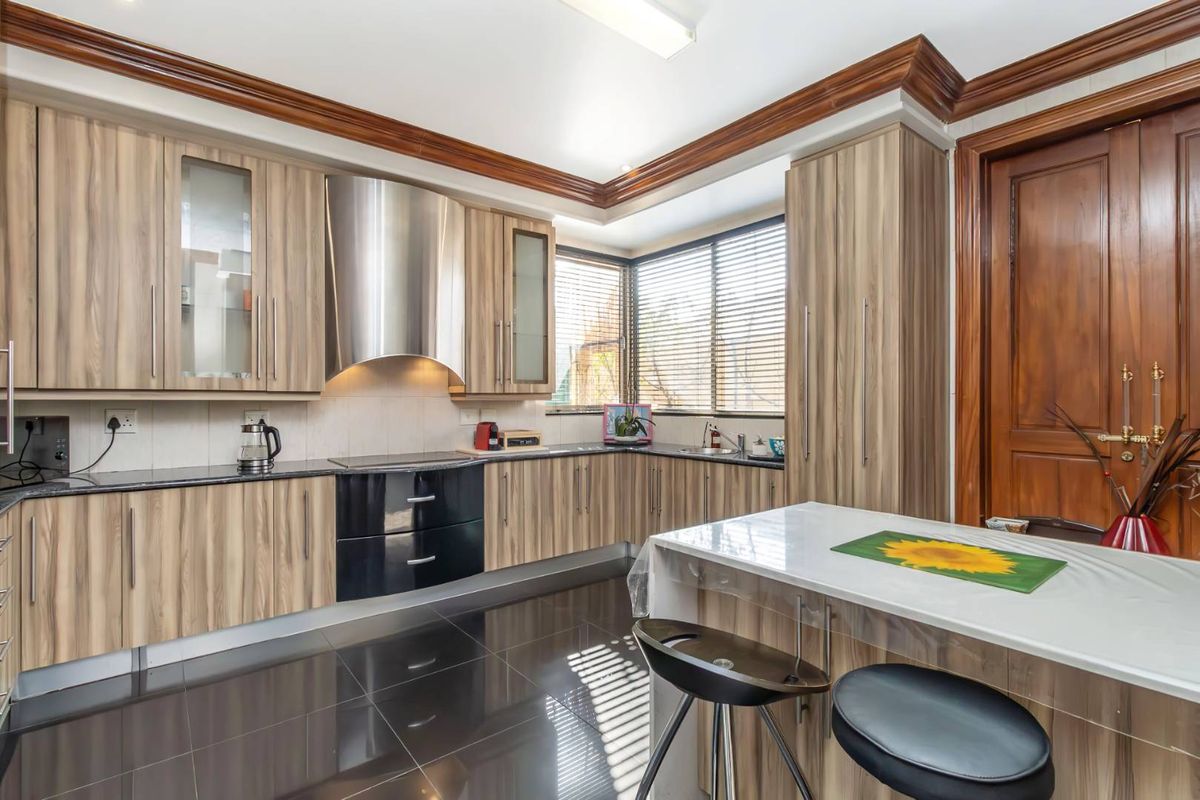 A well-maintained kitchen featuring wood-grain cabinetry, dark granite countertops, a stainless steel extractor fan, and sleek black floor tiles.