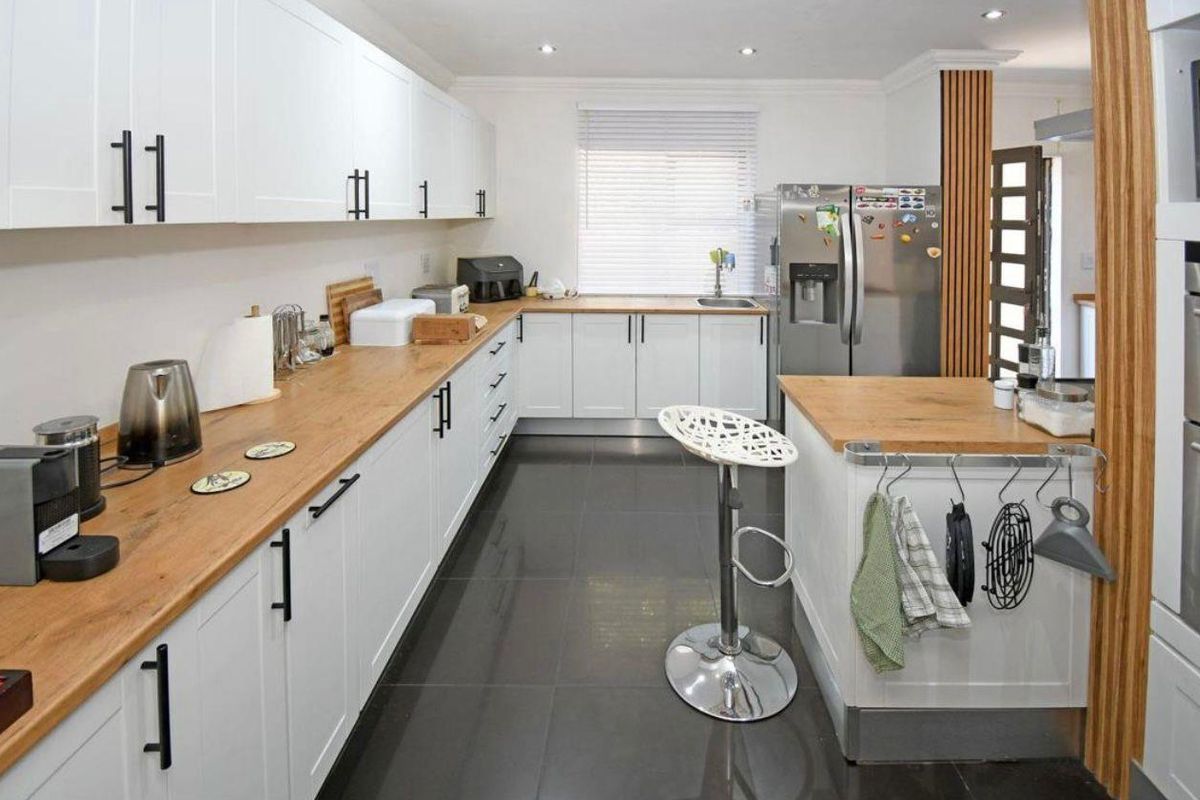 Modern kitchen featuring white shaker cabinetry, warm wooden countertops, dark tiled flooring, and integrated appliances with stylish wood-paneled accents.