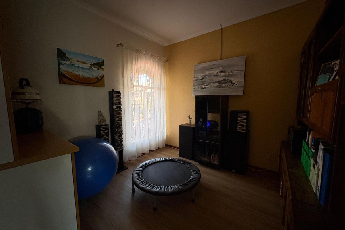 A bedroom featuring laminate flooring, a window with sheer curtains, and neutral wall finishes, suitable for use as a guest room or home office.