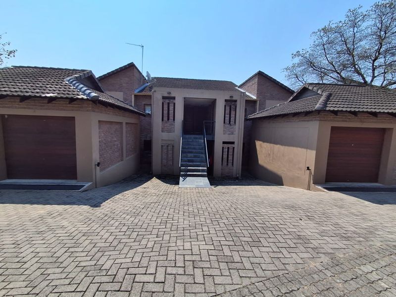 Front exterior view of the apartment complex featuring a paved driveway, double garage doors, and a central staircase leading to the entrance.