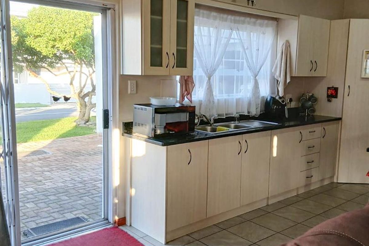 A functional kitchen area featuring light-toned cabinetry, a double sink, and direct access to an outdoor patio through a sliding glass door.