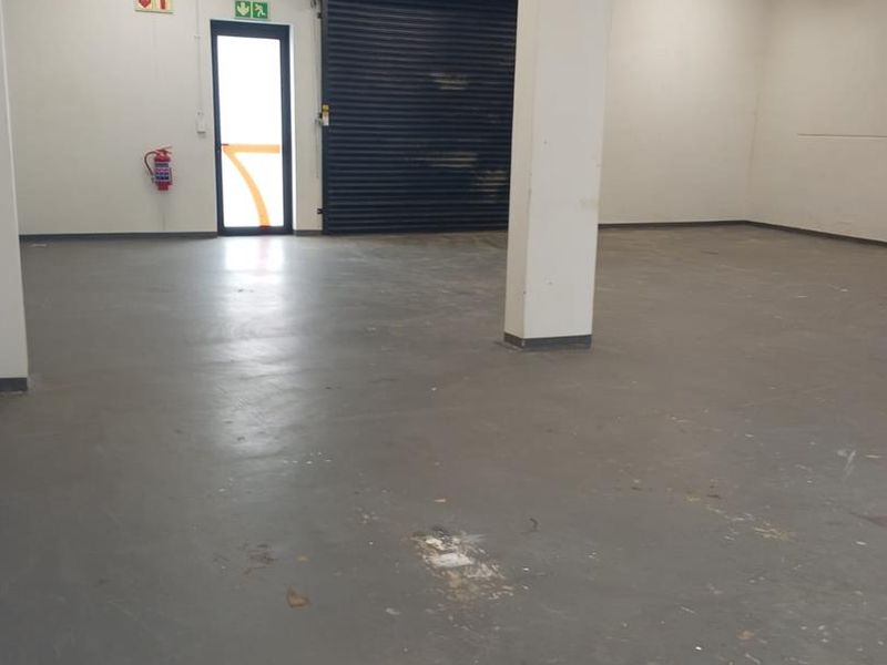Spacious industrial utility area featuring concrete flooring, exposed cable management, and a secure roller shutter door access point.