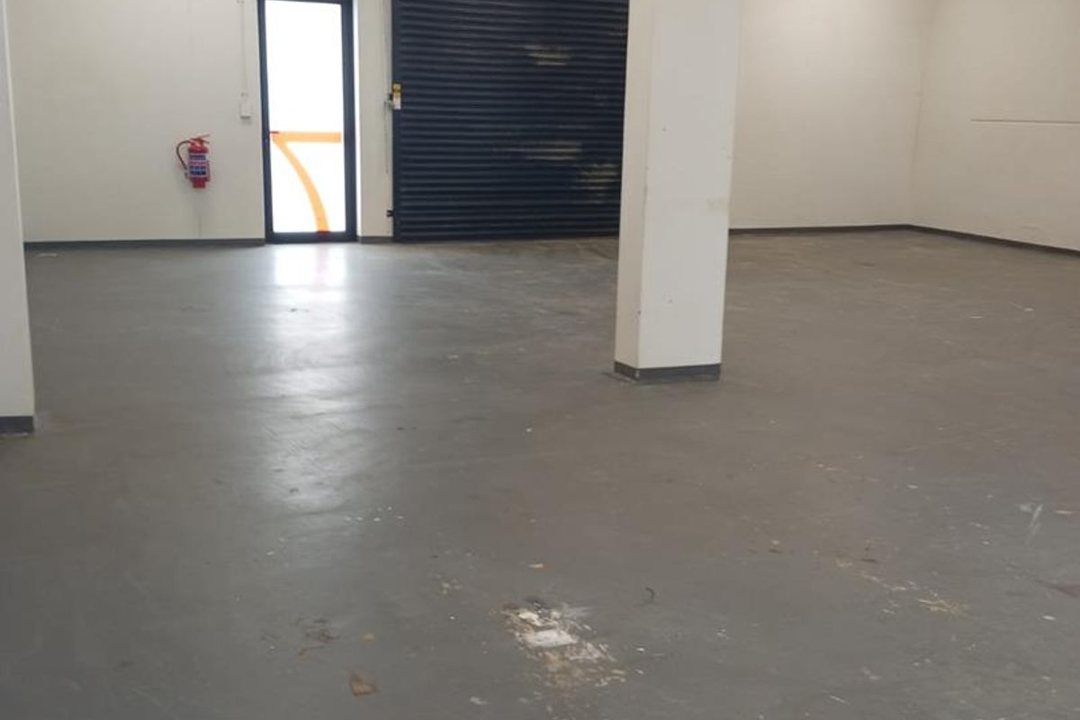 Spacious industrial utility area featuring concrete flooring, exposed cable management, and a secure roller shutter door access point.