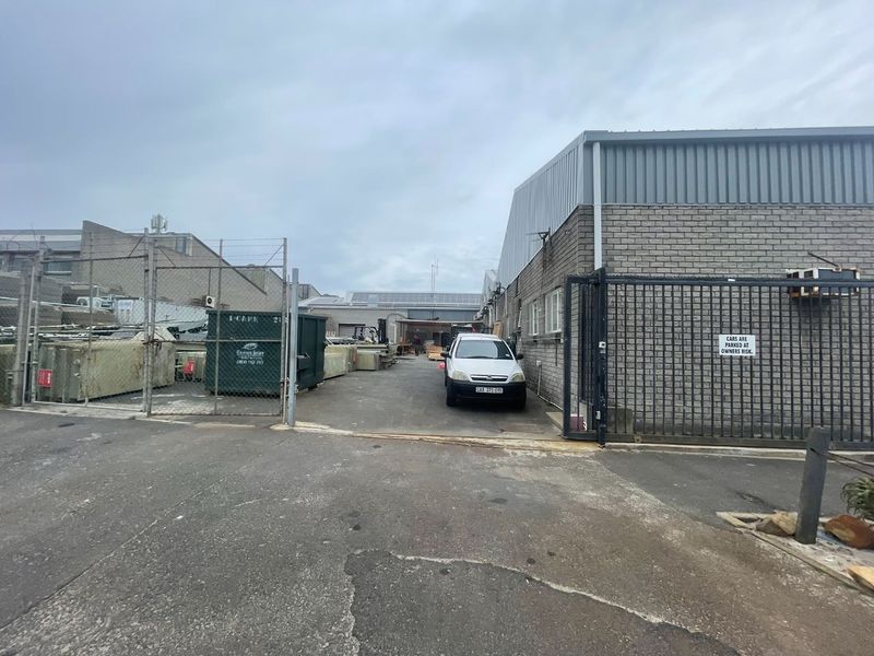 Rear industrial yard area featuring a secure gated entrance, brick and metal building facade, and paved driveway access.