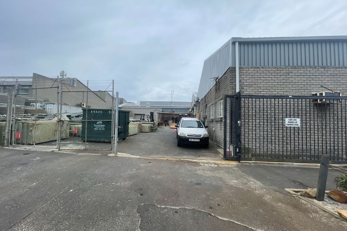 Rear industrial yard area featuring a secure gated entrance, brick and metal building facade, and paved driveway access.