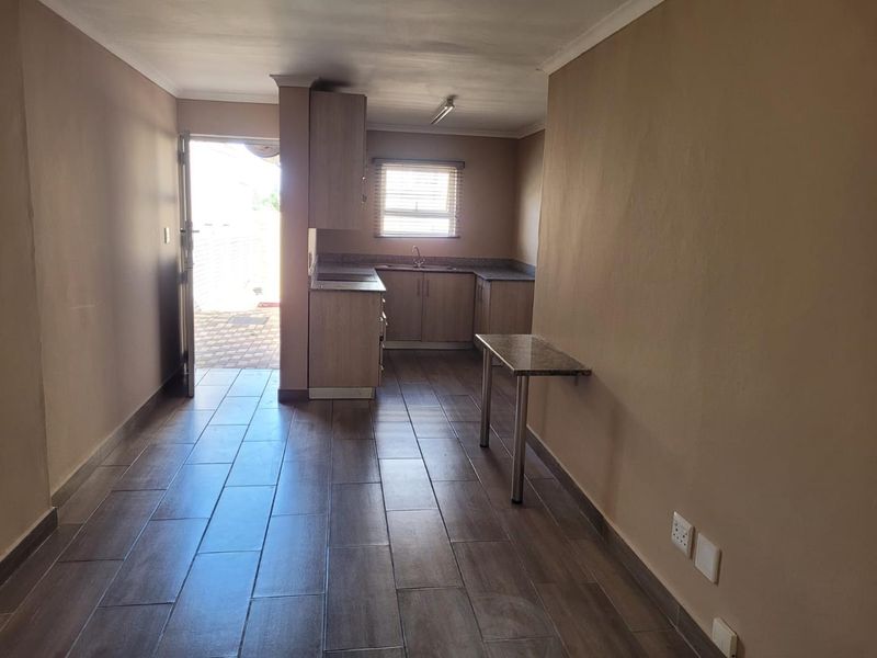 A functional kitchen area featuring built-in cabinetry, laminate countertops, a stainless steel sink, and tiled flooring, with direct access to the exterior.