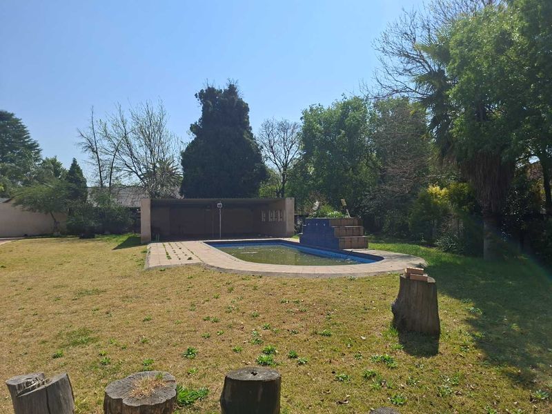 Outdoor pool area featuring a swimming pool with a water feature and an adjacent covered patio space set within a large garden.