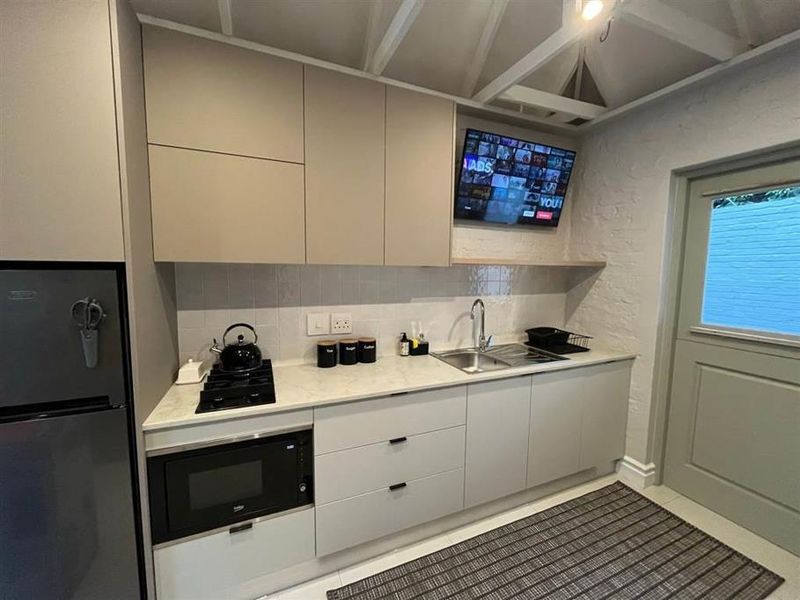Modern kitchen featuring sleek cabinetry, stone countertops, gas hob, built-in microwave, and exposed beam ceiling with direct access to the exterior.