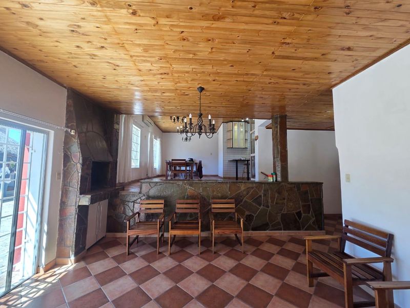Spacious open-plan living area featuring a built-in stone fireplace, stone-clad breakfast bar, timber ceiling, and terracotta tiled flooring with access to the outdoors.